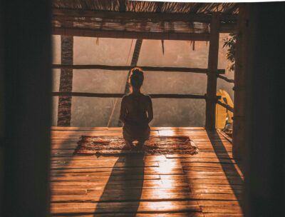 Woman practicing the 4-7-8 Breathing Method on her knees on a wooden floor, surrounded by nature.