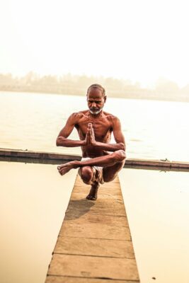 A man practicing yoga asanas on a dock by the water.