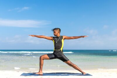 A man practicing Ashtanga Yoga poses on the beach at sunrise.