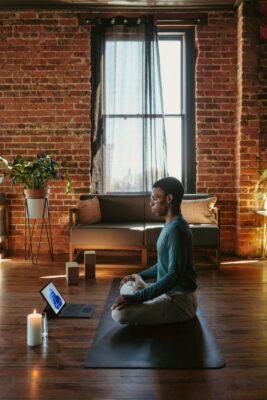 Man sitting on a yoga mat in a living room preparing to practice box breathing exercises.