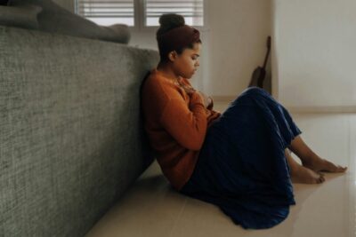 A woman sitting on the floor with her hands resting on her chest, struggling with anxiety and needing breathing exercises for relief.