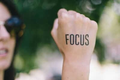 A woman holding her back hand with the word 'Focus' written, representing breathing techniques for mental clarity and concentration.