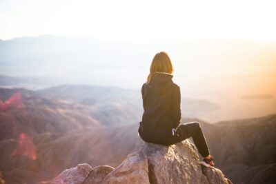 A woman practicing breathing exercises for mental clarity while sitting on a mountaintop.