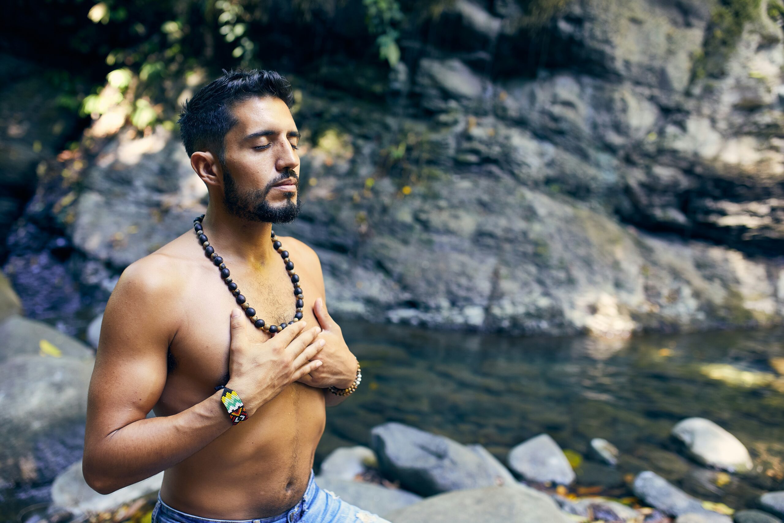 A man practicing breathing exercises for mindfulness in nature, surrounded by water and rocks.