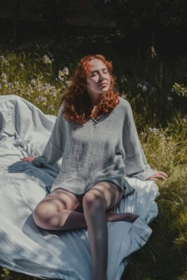 A woman sitting on a white textile in nature, practicing breathing for relaxation and stress relief.