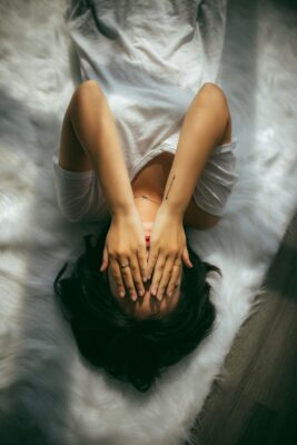 A woman lying in bed with her hands covering her face, in need of breathing exercises for stress relief.