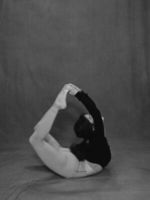 A woman practicing Dhanurasana Pose, also known as Bow Pose, on a yoga mat.