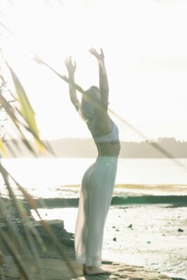 A woman stands by the sea with her arms wide open, embracing the relaxing environment and experiencing a deep sense of health and wellness.