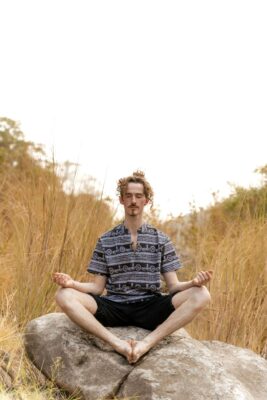 Man practicing Pranayama Bhramari on a rock in a peaceful field