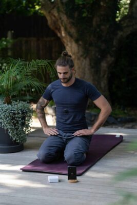 Man practicing Pranayama sitting on a yoga mat with hands on waist.