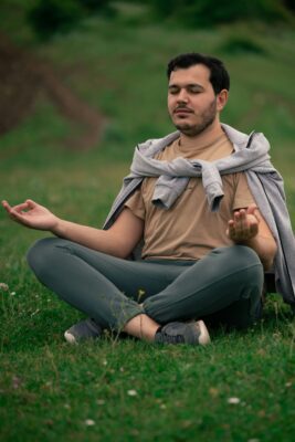 Man practicing the Wim Hof Breathing Method in a yoga pose, seated on grass surrounded by nature.